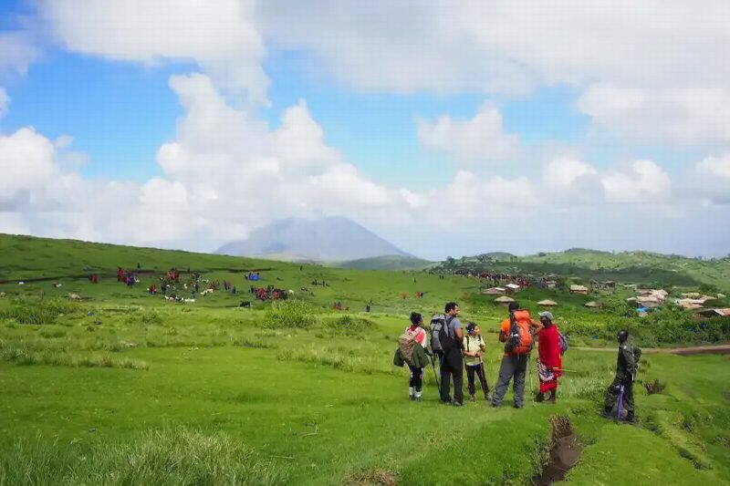 Walkers crossing rolling green highland pasture below a line of hills.