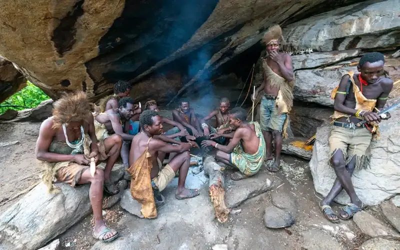 A group of Hadzabe men sitting around a fire in a rock shelter.