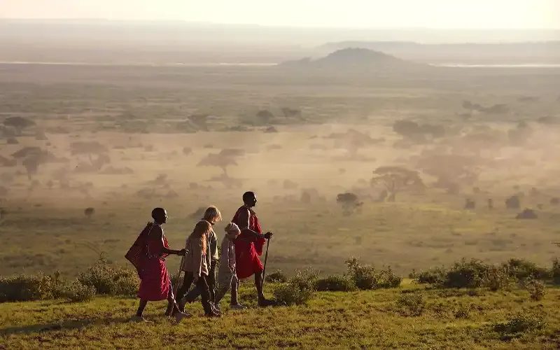Three Maasai men in red shukas walking across a misty plain.