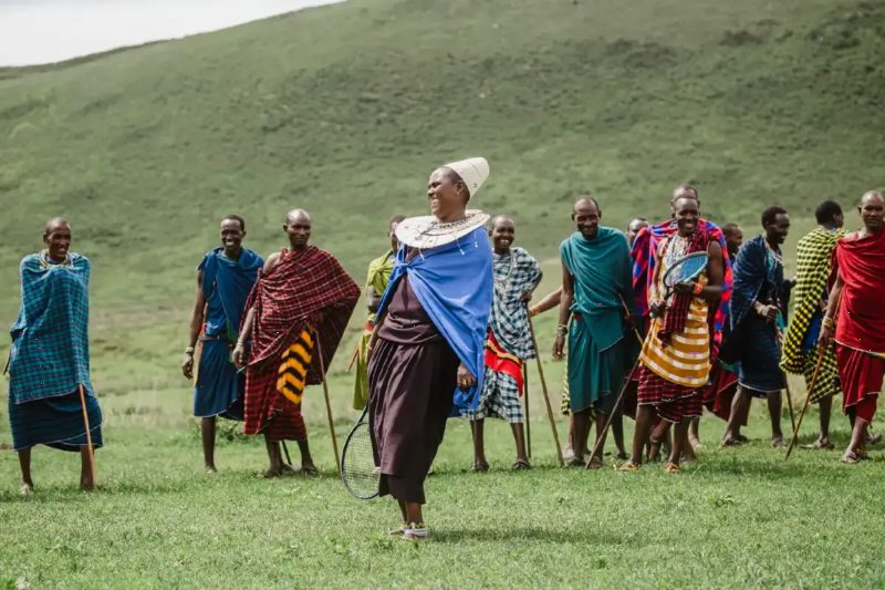 A visitor walking with Maasai men and women in bright shukas on a green hillside.