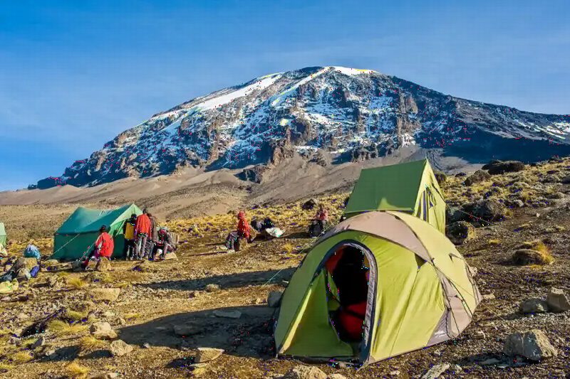 Green and yellow tents in a high camp below the snow-streaked summit of Kibo.