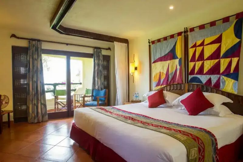 A lodge bedroom with a large bed, a patterned bedcover and bright wall hangings.