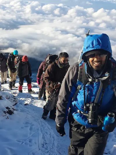 A climber in a blue jacket and goggles on a snowy path near the summit.