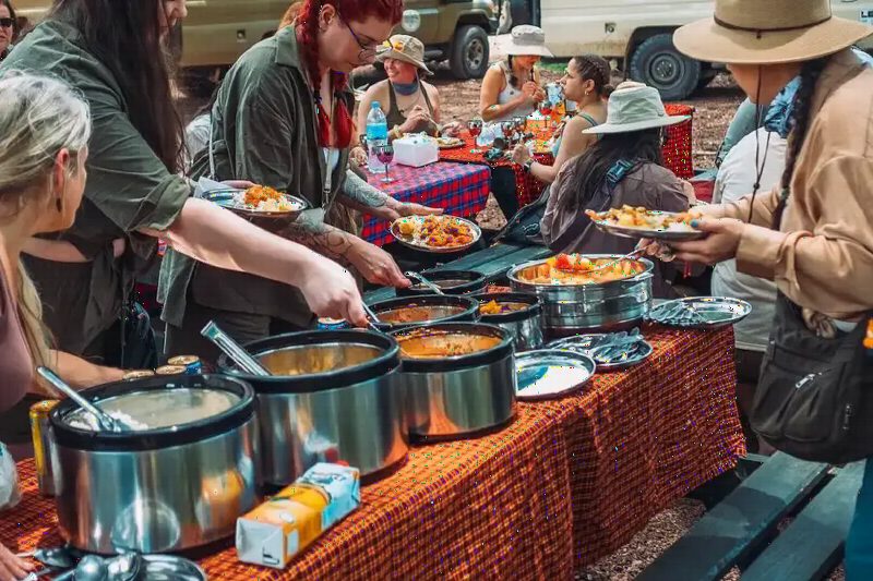 Travellers helping themselves to local dishes from steaming pots at an outdoor buffet.