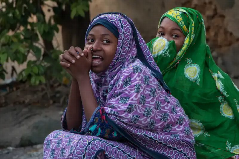 Two women in bright headscarves, one smiling at the camera.